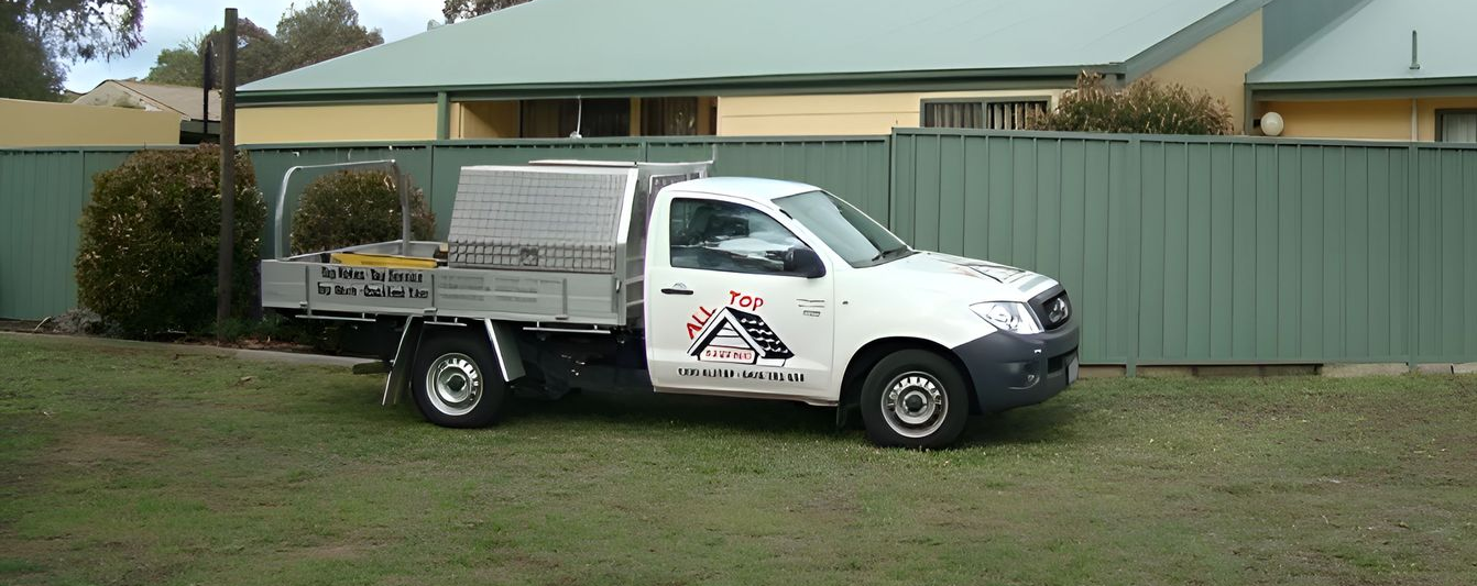 White pickup truck parked on grass, in front of a green fence and yellow house — All Top Roofing In Royalla, NSW