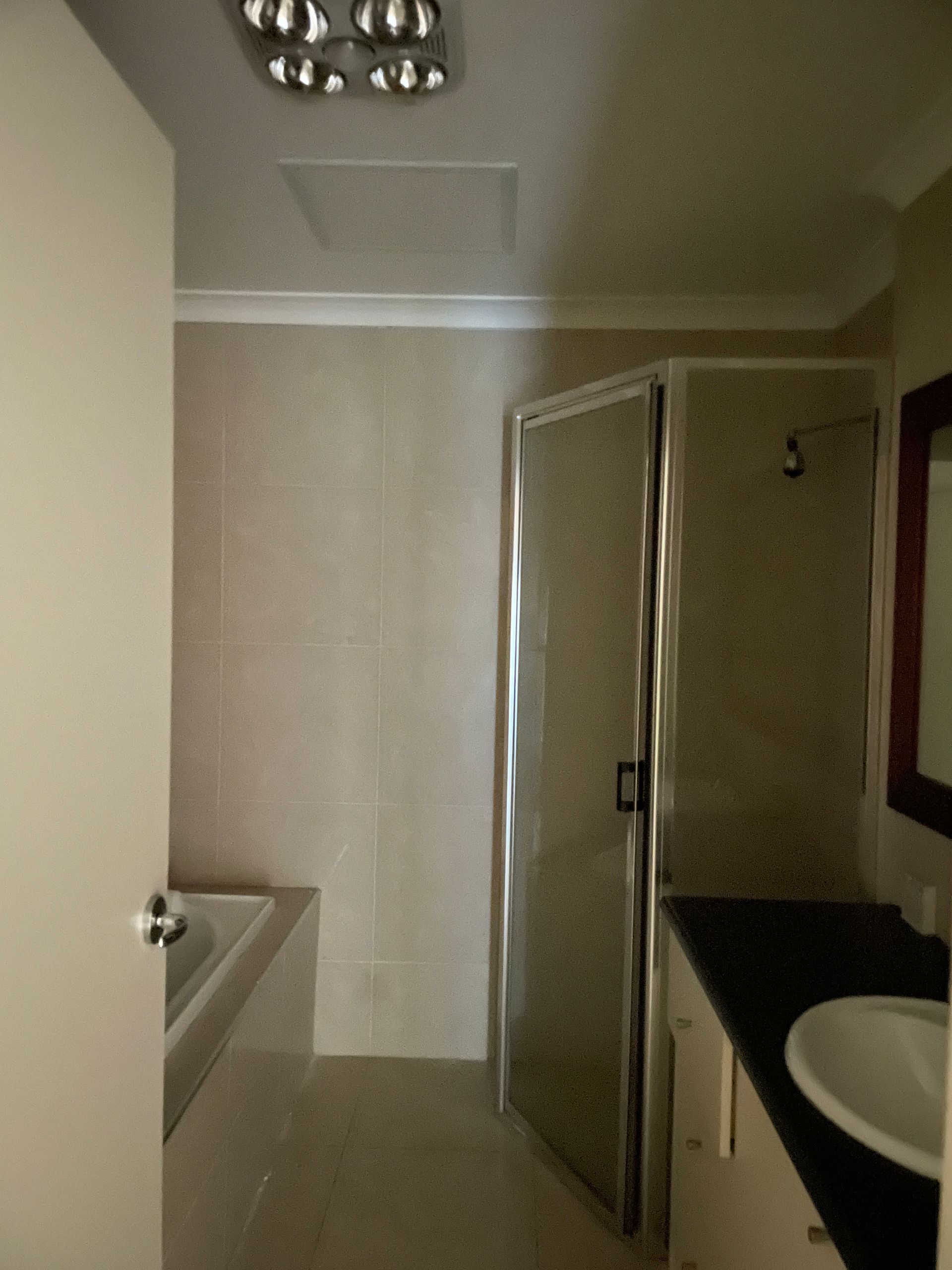 Bathroom with shower, vanity, and tub. Light walls, dark countertop, and white fixtures — All Top Roofing In Royalla, NSW