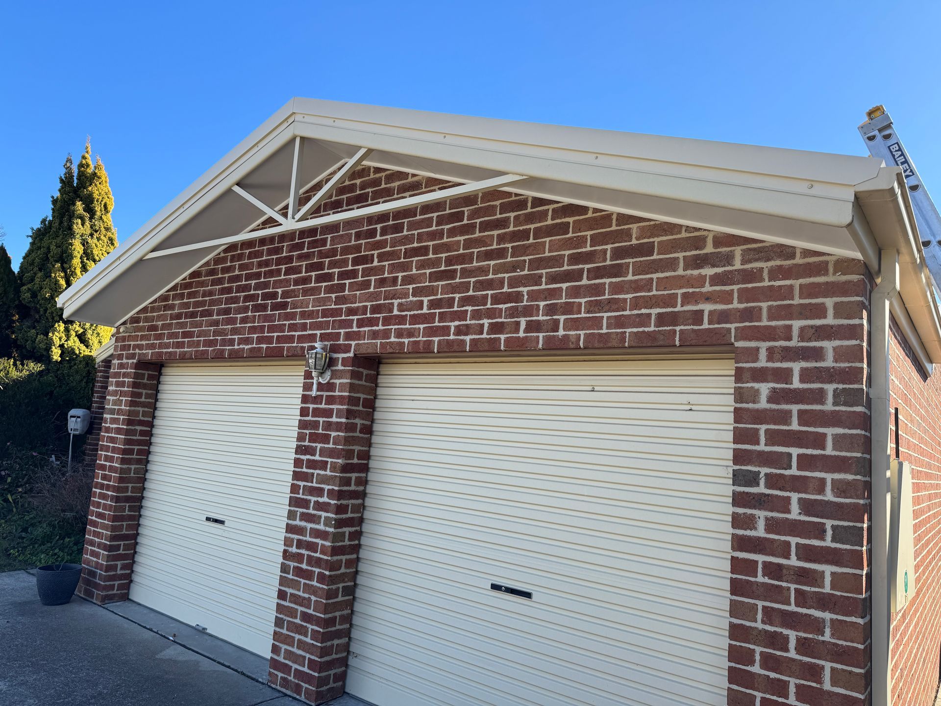 Brick garage with cream-coloured roller doors and roof, against a blue sky — All Top Roofing In Tuggeranong, ACT