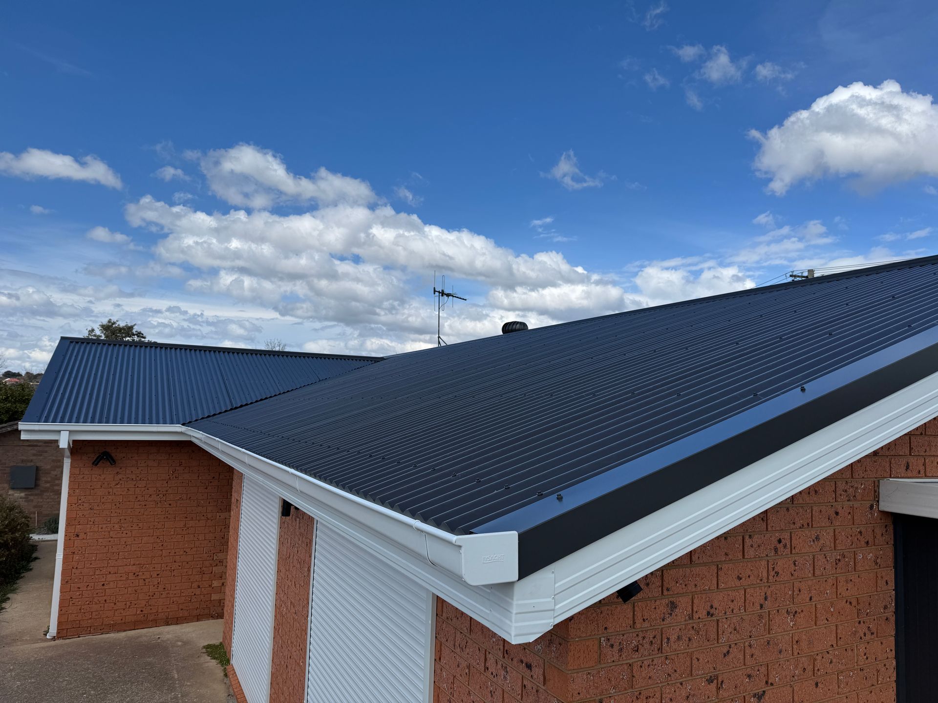 A white gutter on the side of a house with a red roof — All Top Roofing In Royalla, NSW