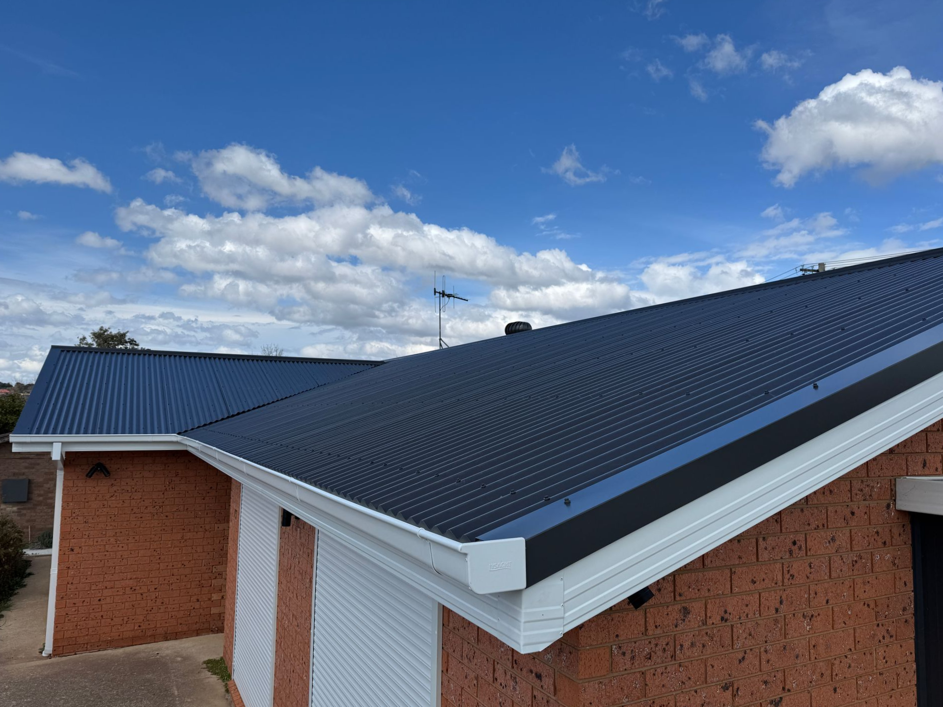 Brick house with dark blue corrugated metal roof against a blue sky with clouds — All Top Roofing In Tuggeranong, ACT