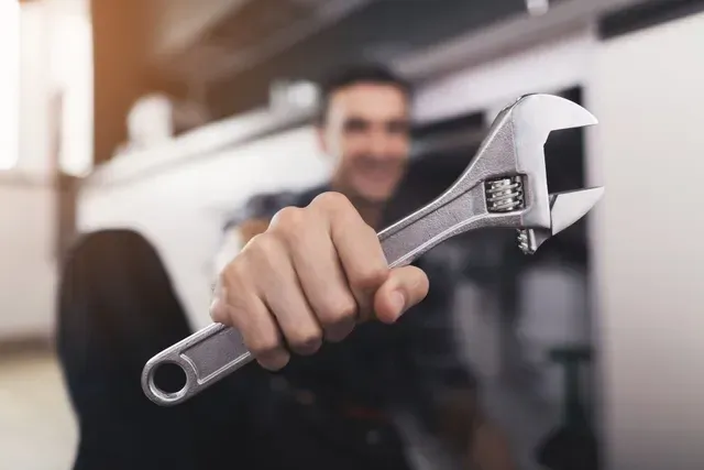 Mécanicien tenant une clé à molette, souriant, dans un garage.