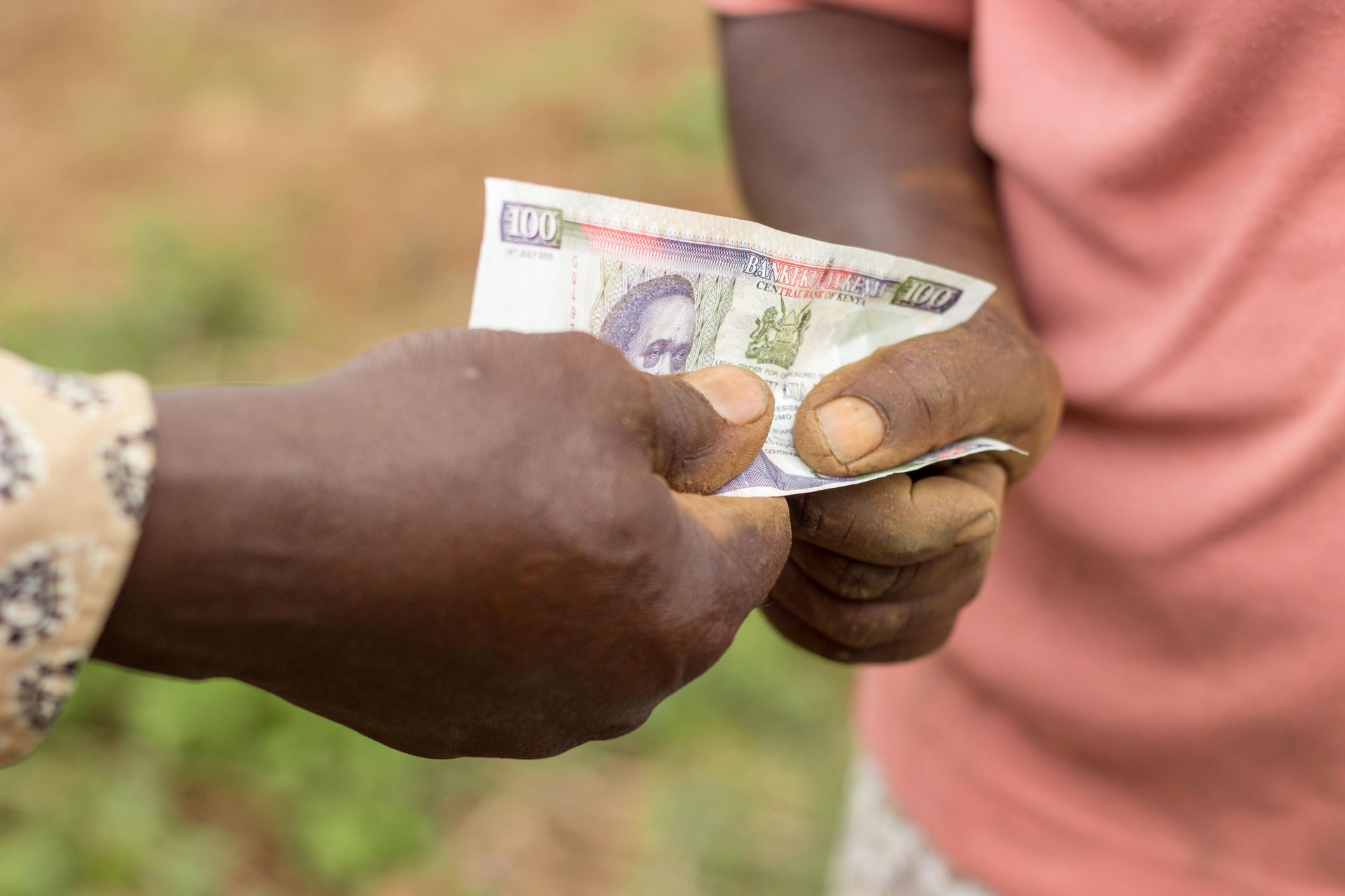 Two hands exchanging a Kenyan 500 shilling banknote.