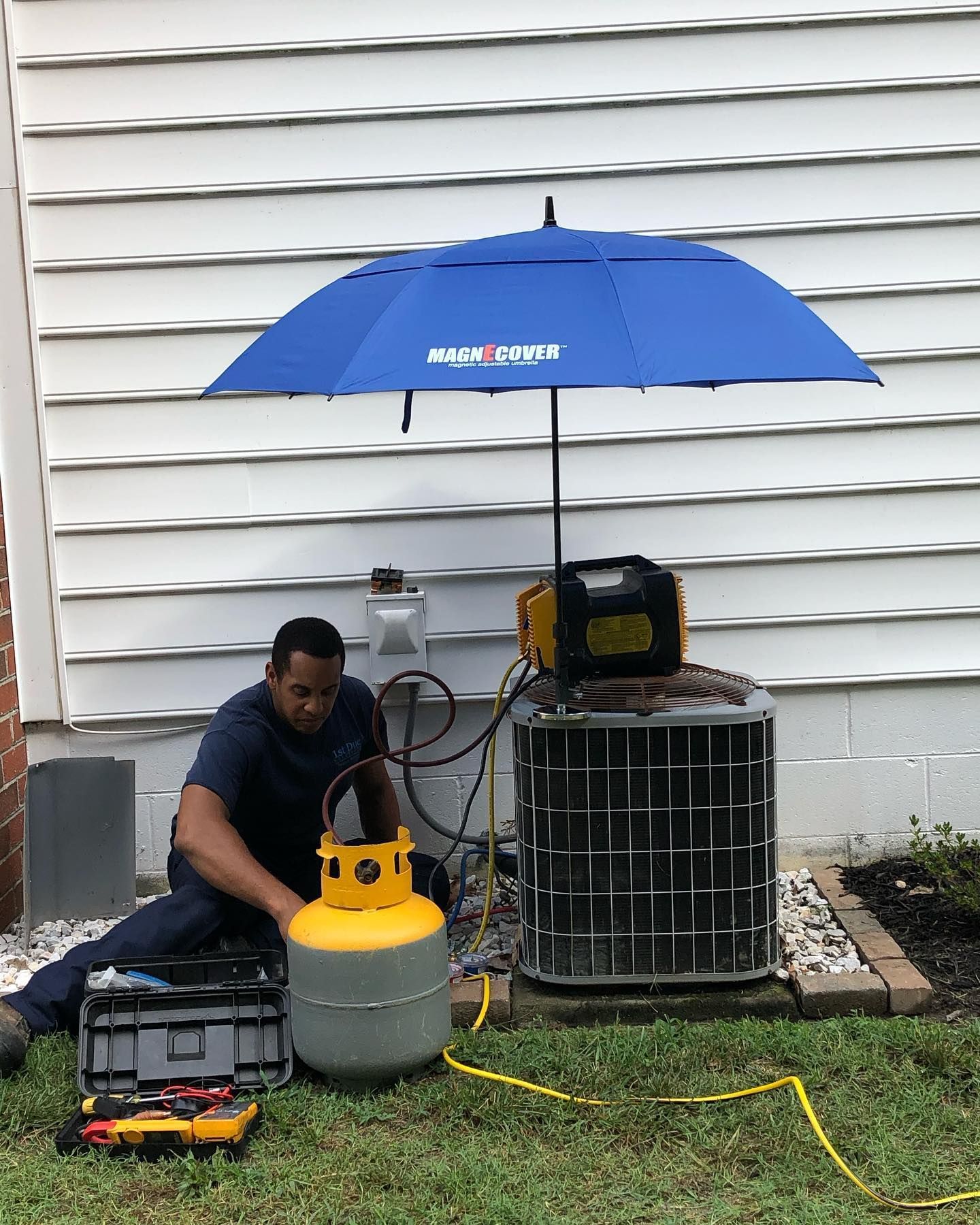 A man is working on an air conditioner under an umbrella.
