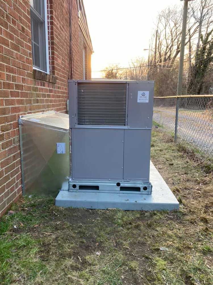A large air conditioner is sitting outside of a brick building.