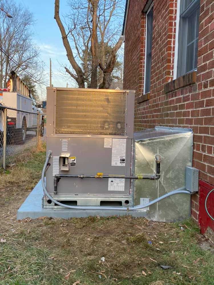 A large air conditioner is sitting on the side of a brick building.