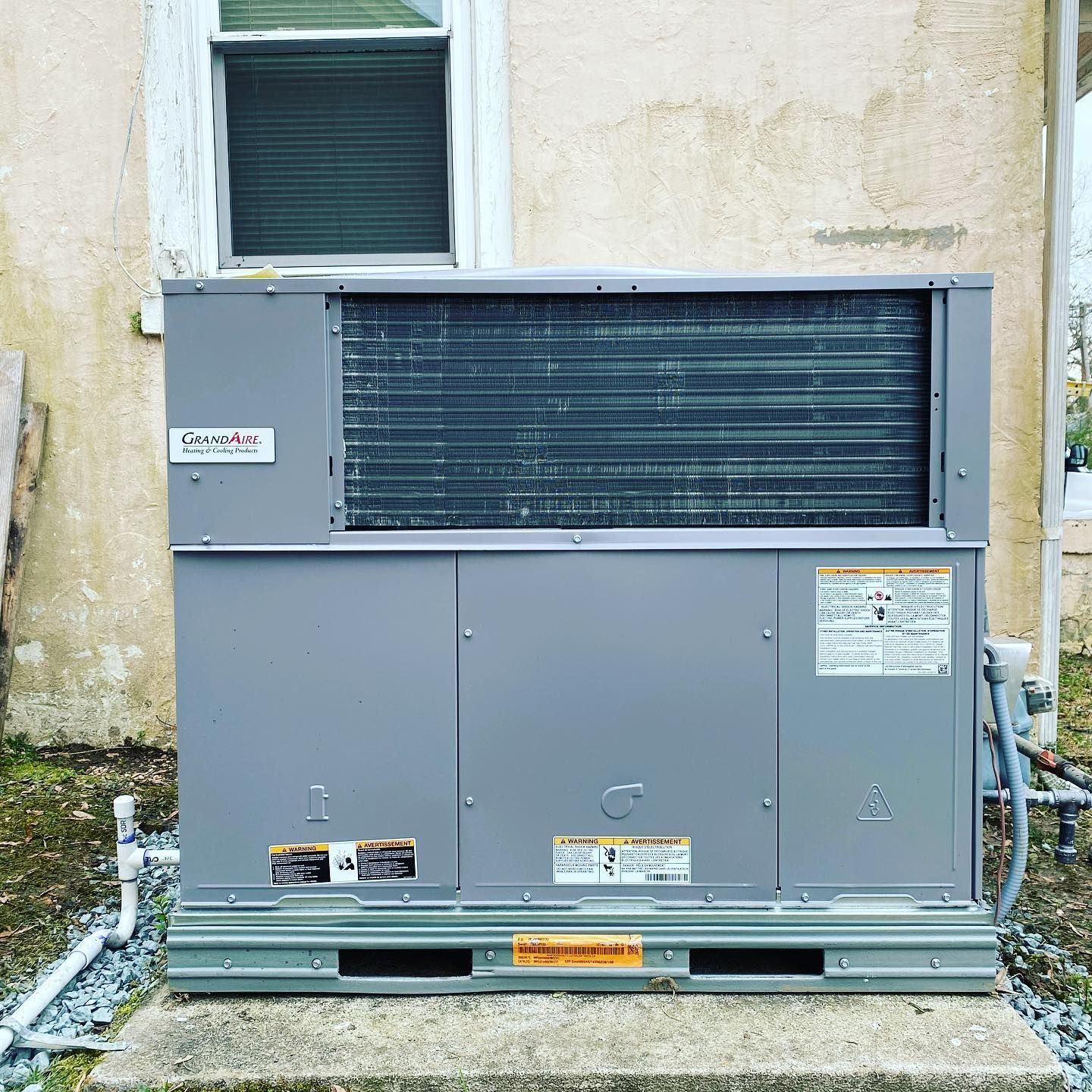 A large air conditioner is sitting outside of a building next to a window.