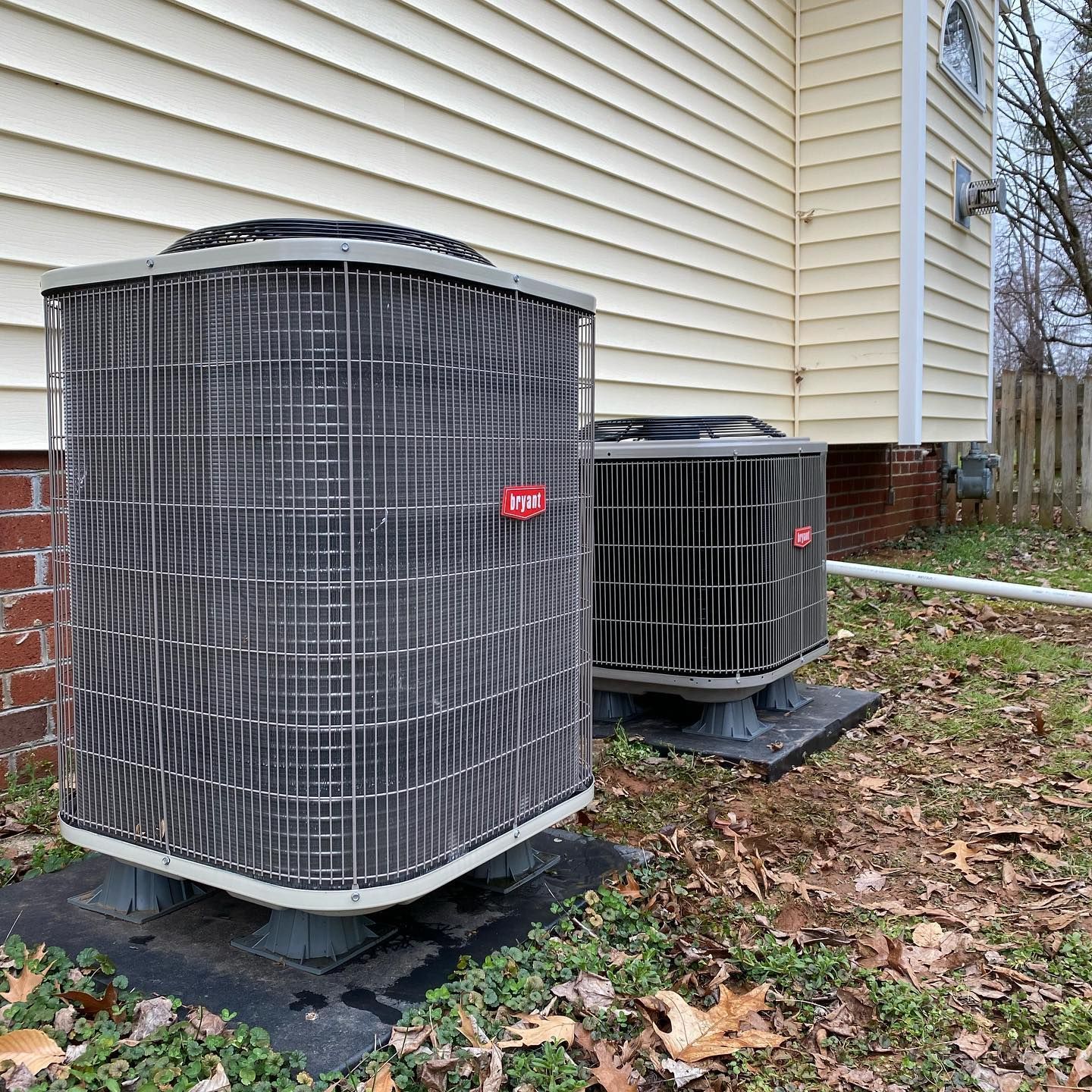 Two air conditioners are sitting on the side of a house.