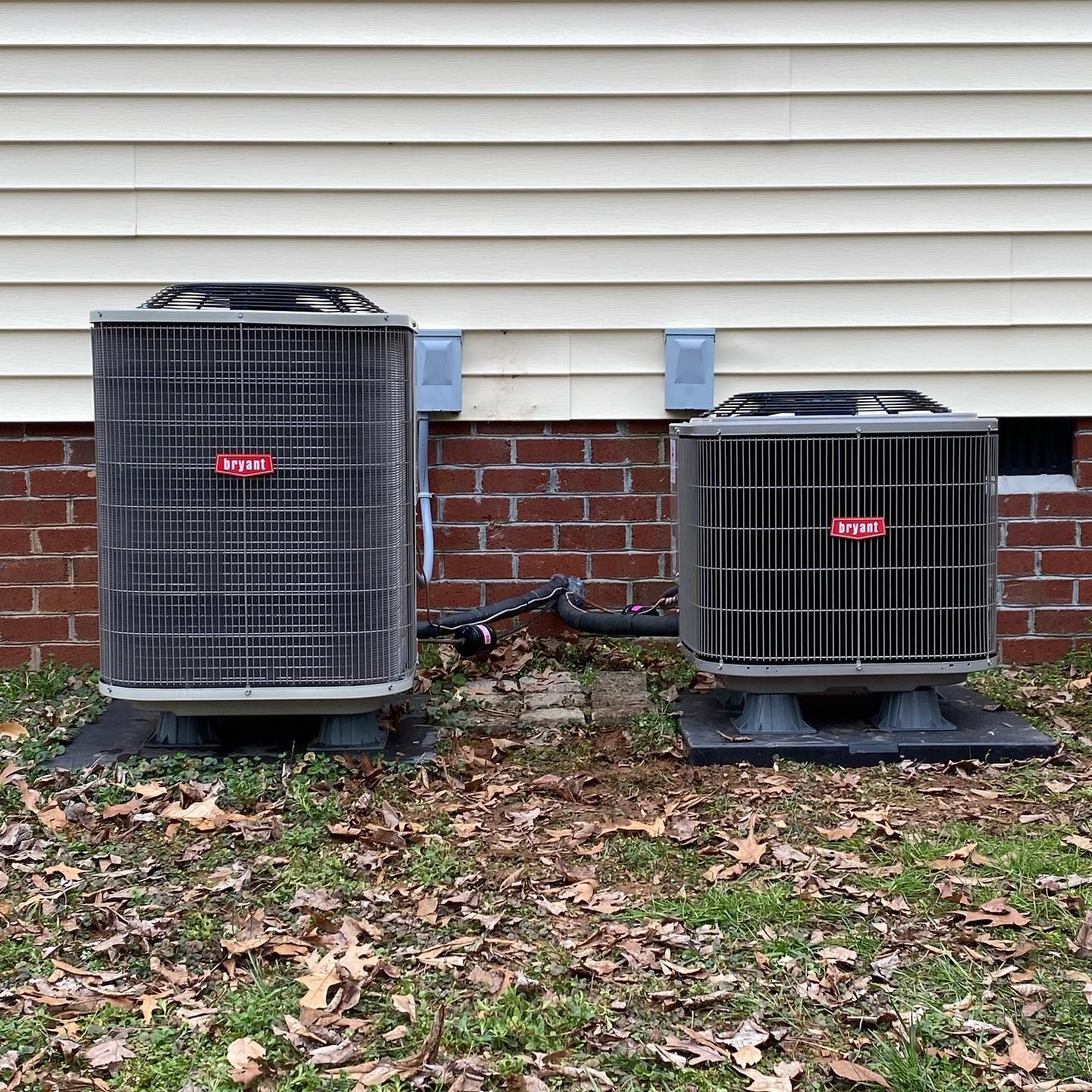 Two air conditioners are sitting next to each other on the side of a house.