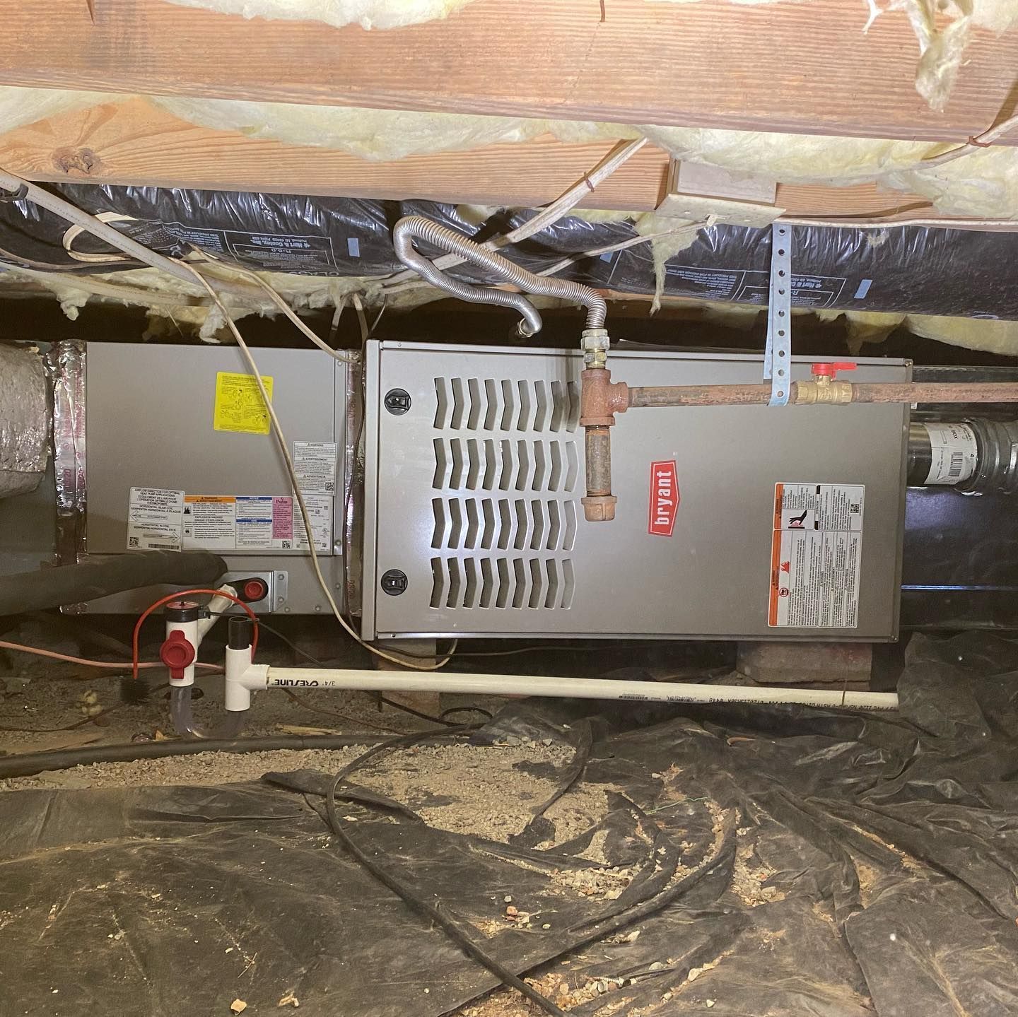 An air conditioner is sitting under a ceiling in a basement.