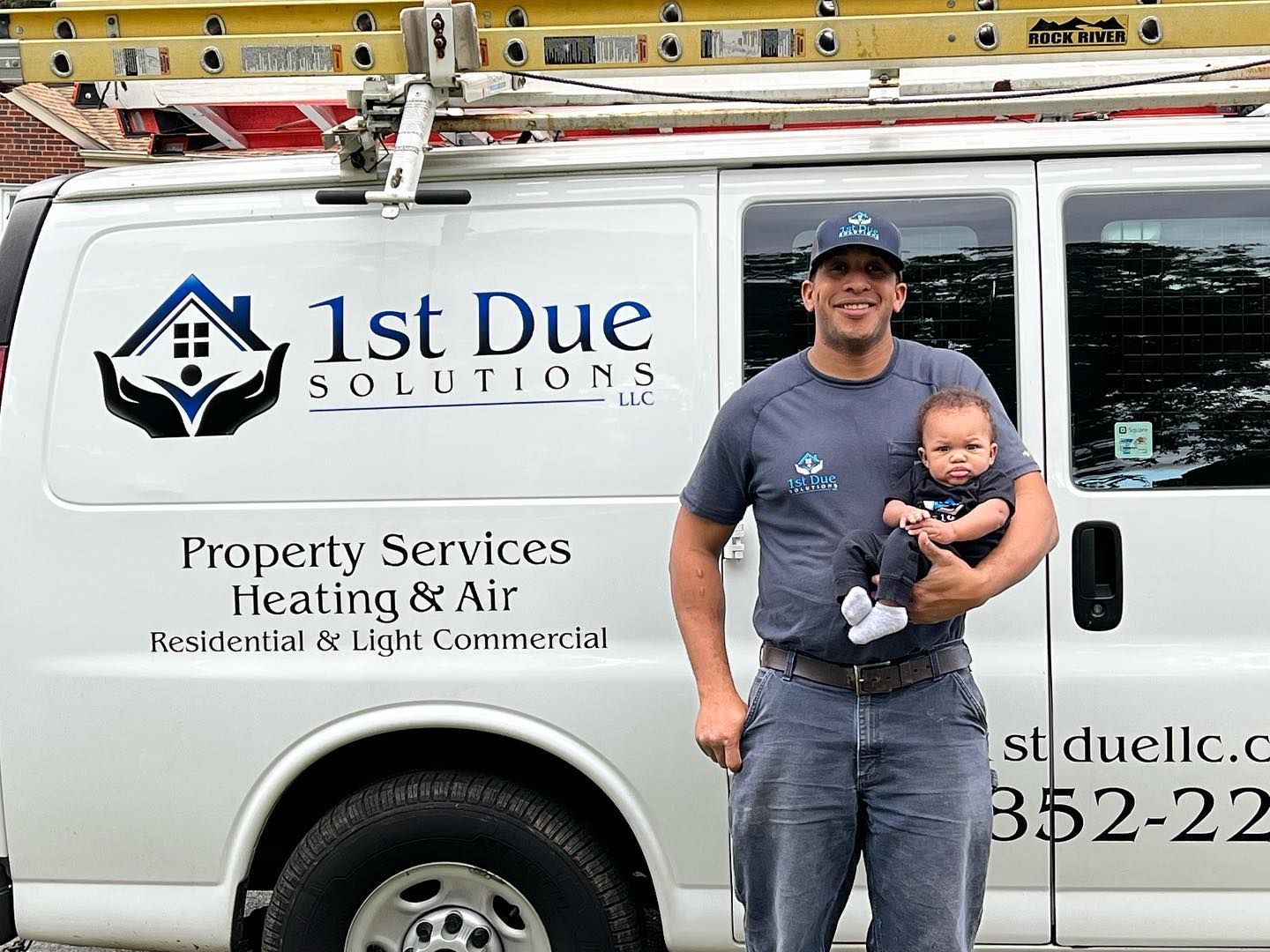 A man is holding a baby in front of a van that says 1st due solutions.
