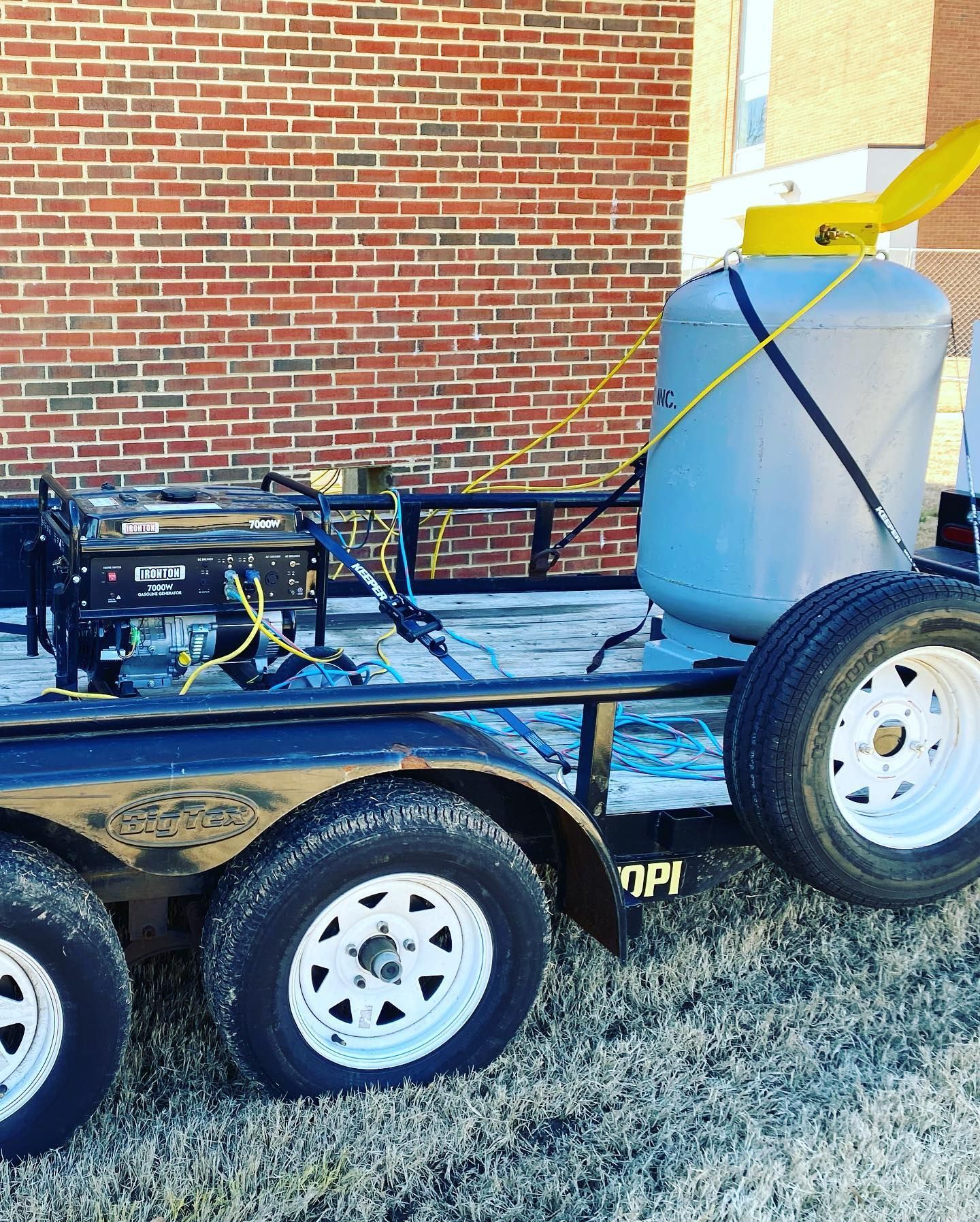 A trailer with a generator on it is parked in front of a brick building.