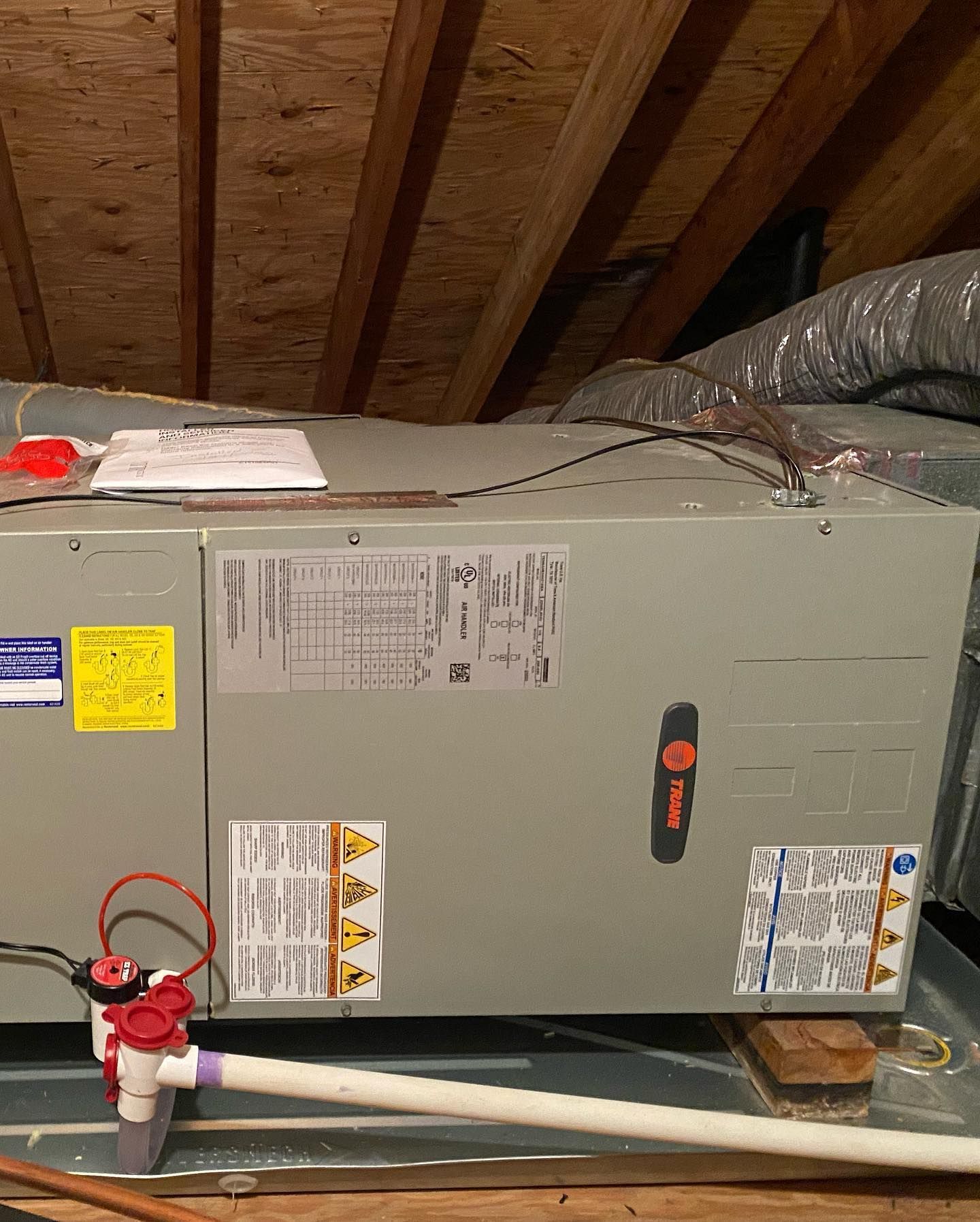 An air conditioner is sitting under a wooden ceiling in an attic.