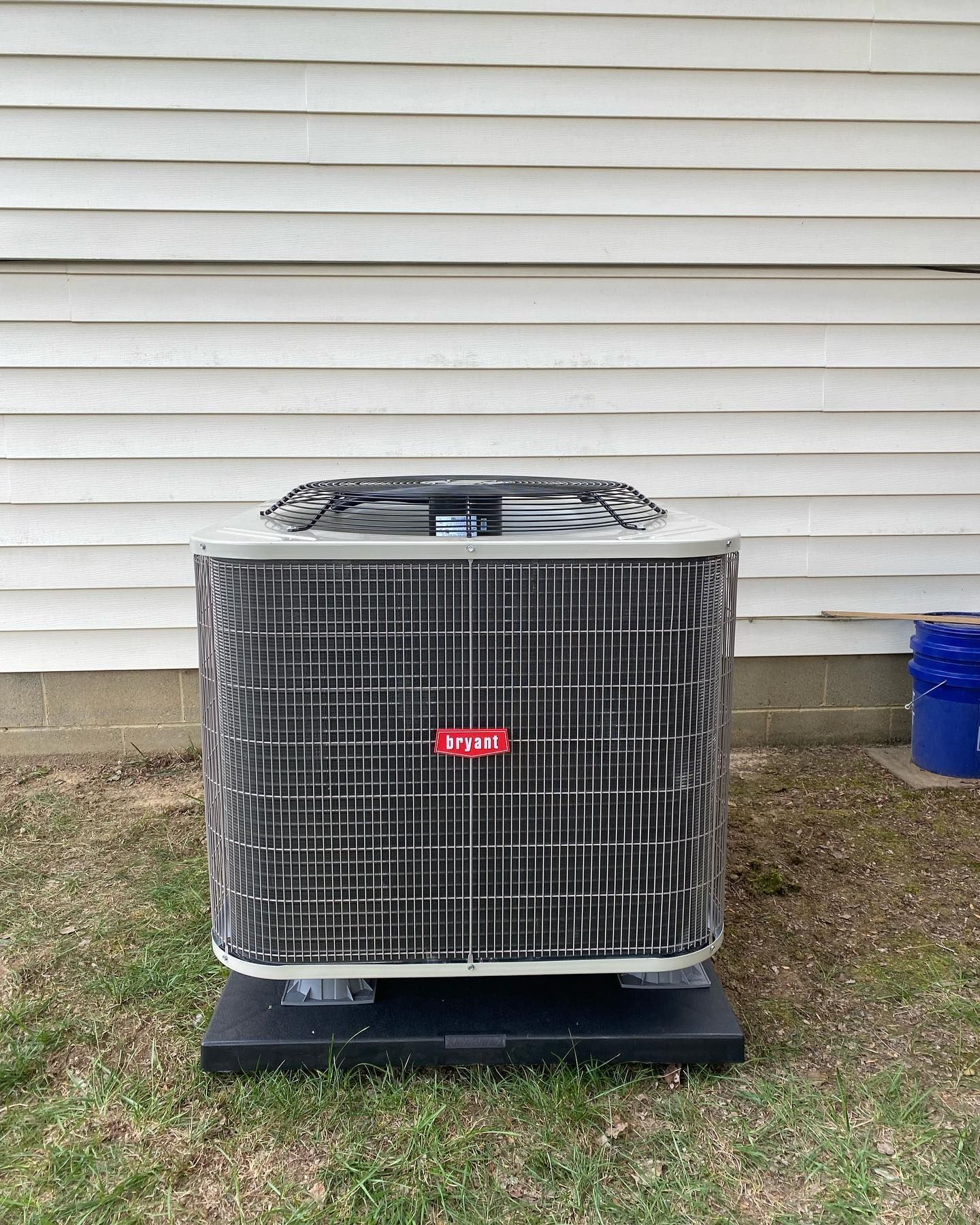 A large air conditioner is sitting in the grass in front of a house.