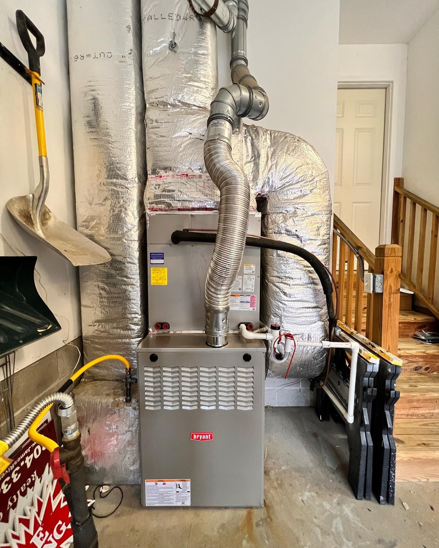 An air conditioner is sitting in a garage next to a shovel