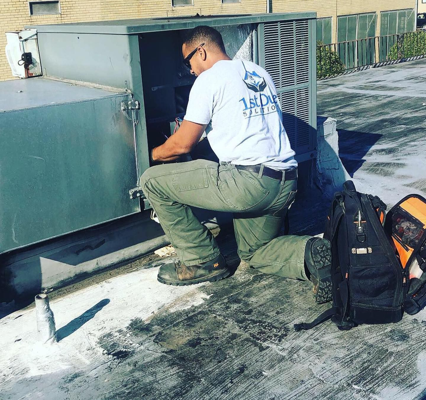 A man is working on an air conditioner on the roof of a building.