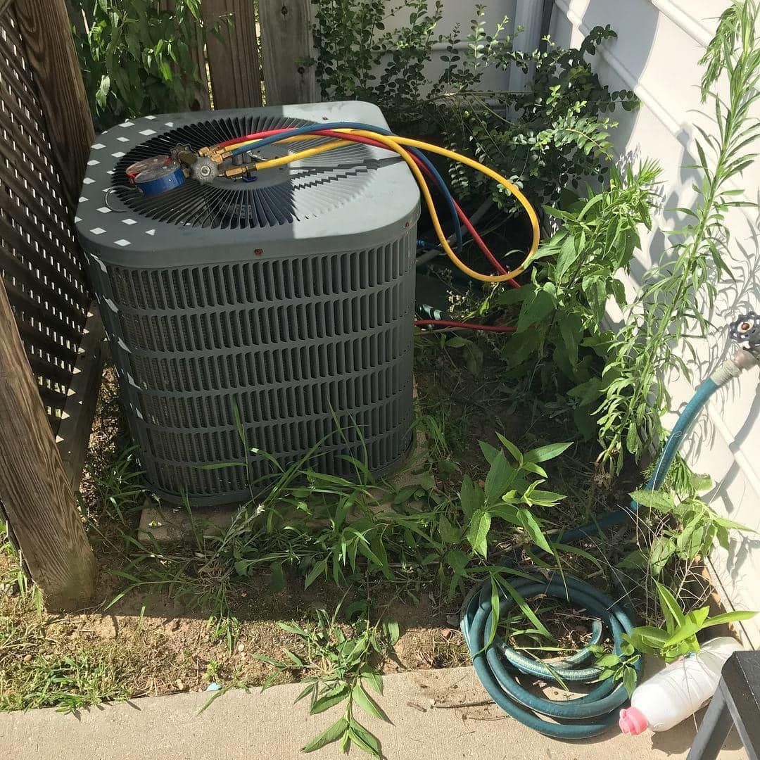 An air conditioner is sitting in the grass next to a hose.
