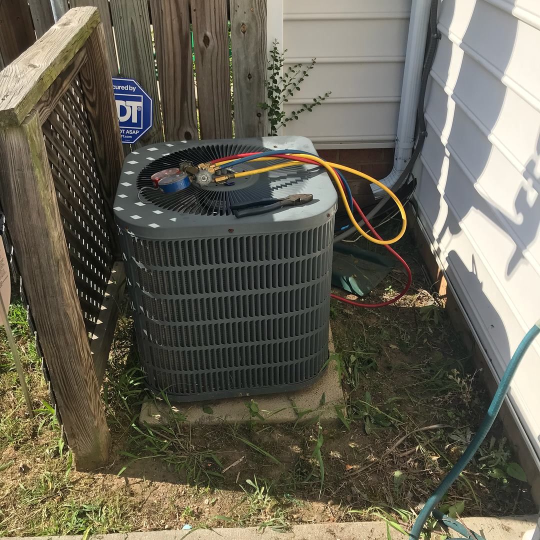 An air conditioner is sitting outside of a house with a hose attached to it.