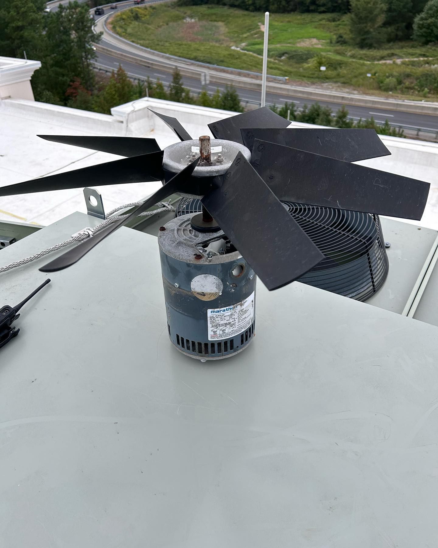 A fan is sitting on top of a roof next to a screwdriver.