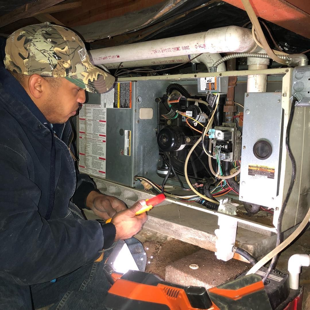 A man is working on an air conditioner in a basement.