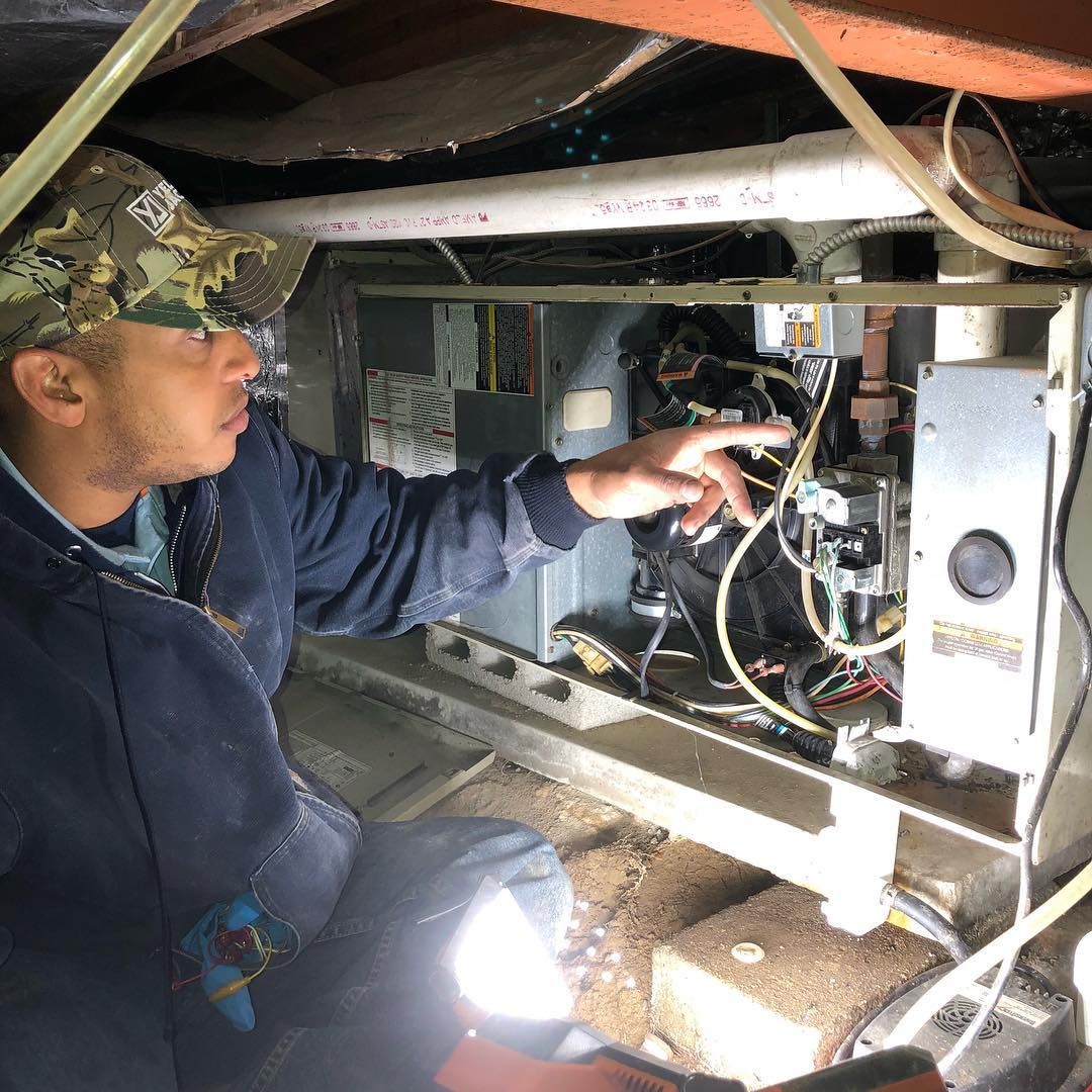 A man is kneeling down in a basement looking at a machine.