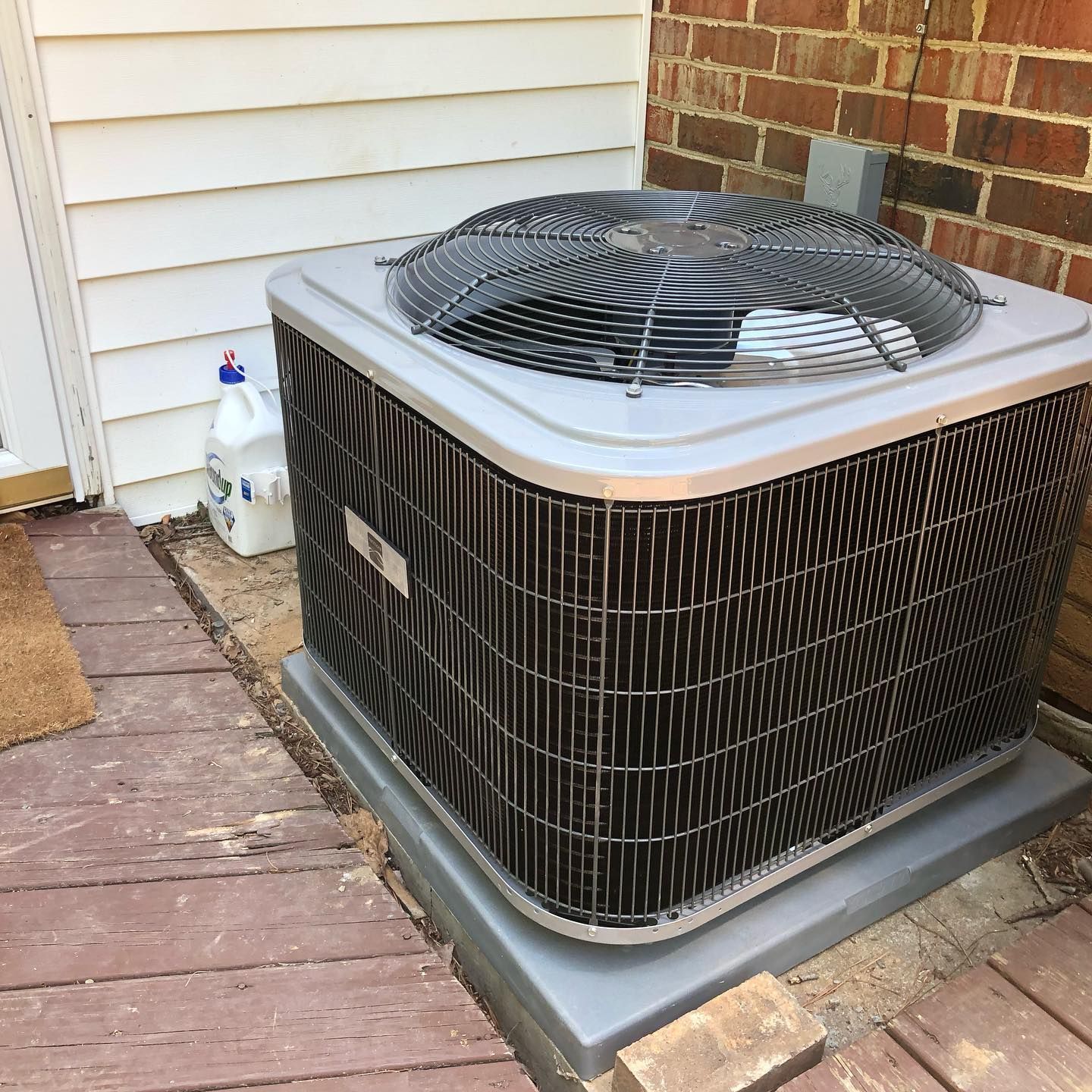 A large air conditioner is sitting outside of a brick house.