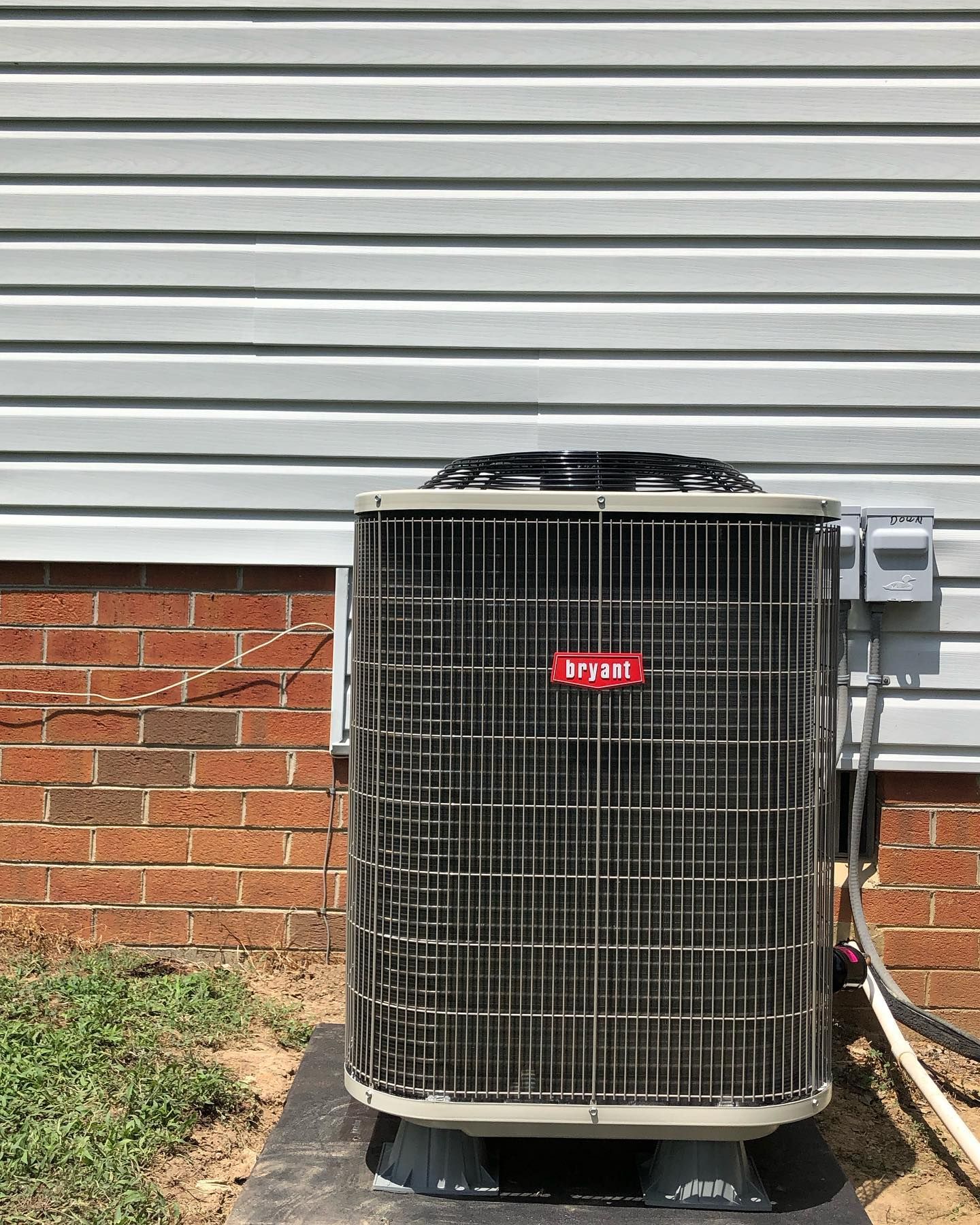 A large air conditioner is sitting outside of a brick house.