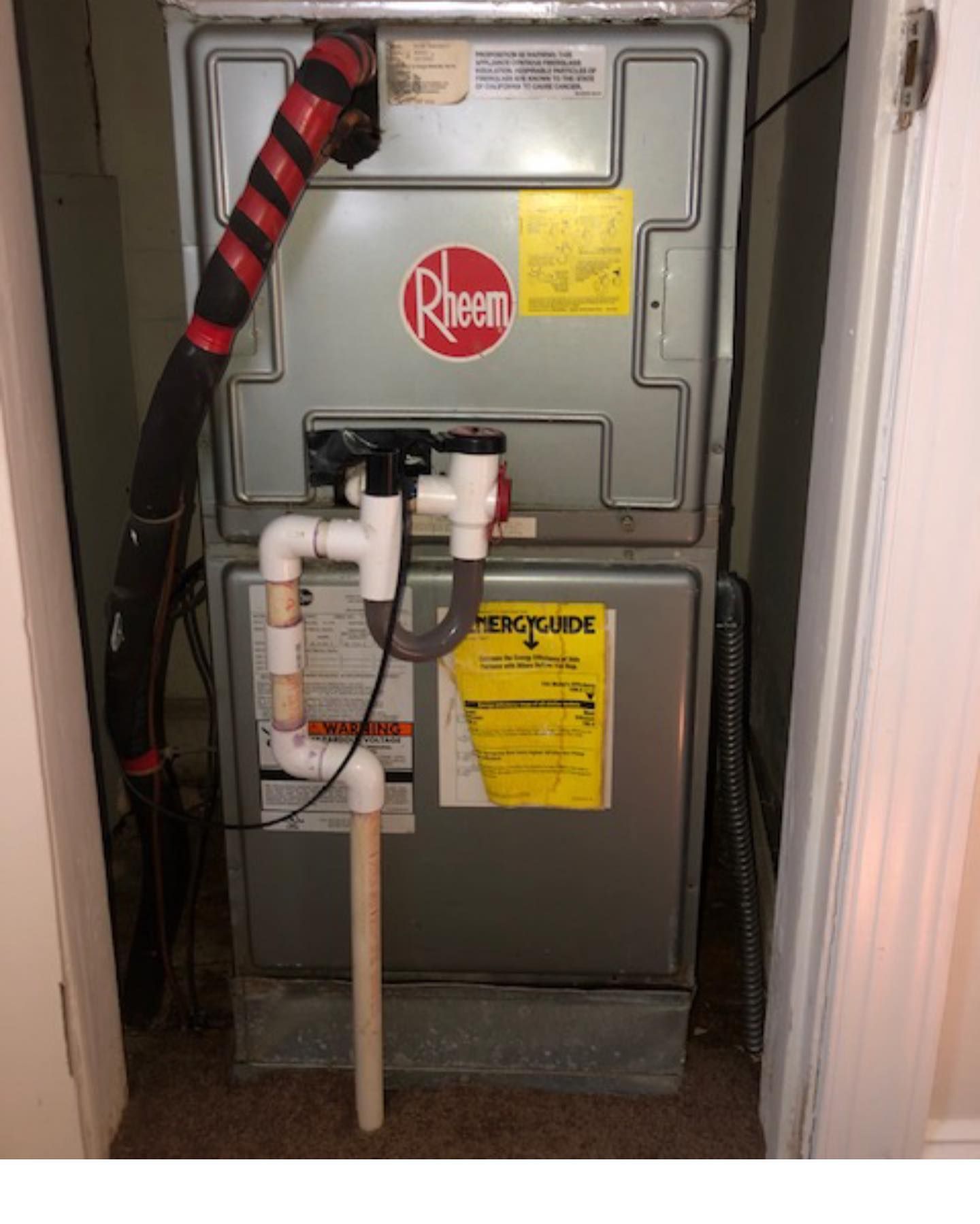 A rheem air conditioner is sitting in a closet next to a door.