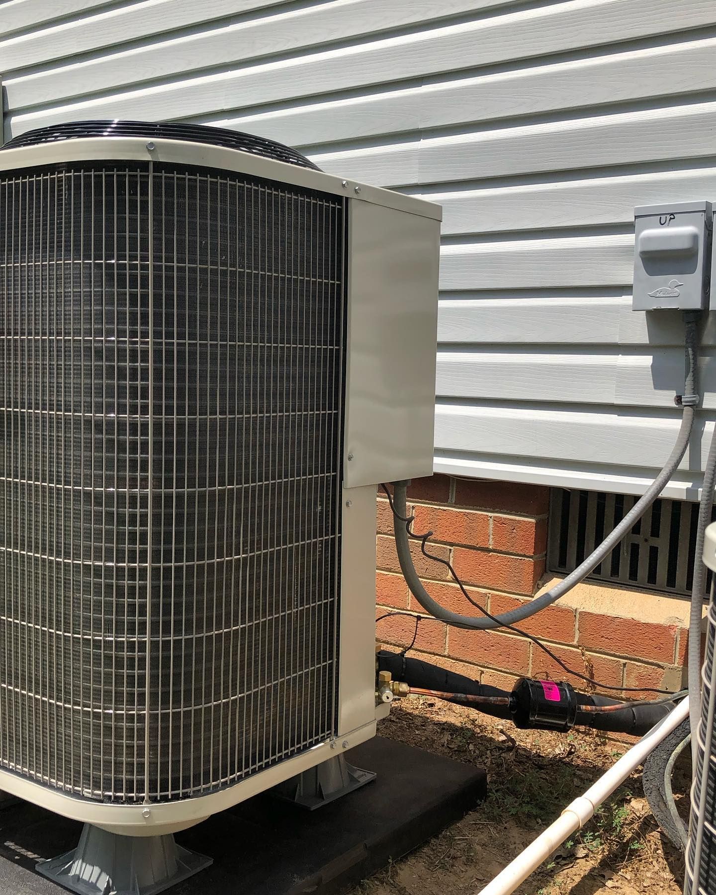 A large air conditioner is sitting outside of a house next to a brick wall.