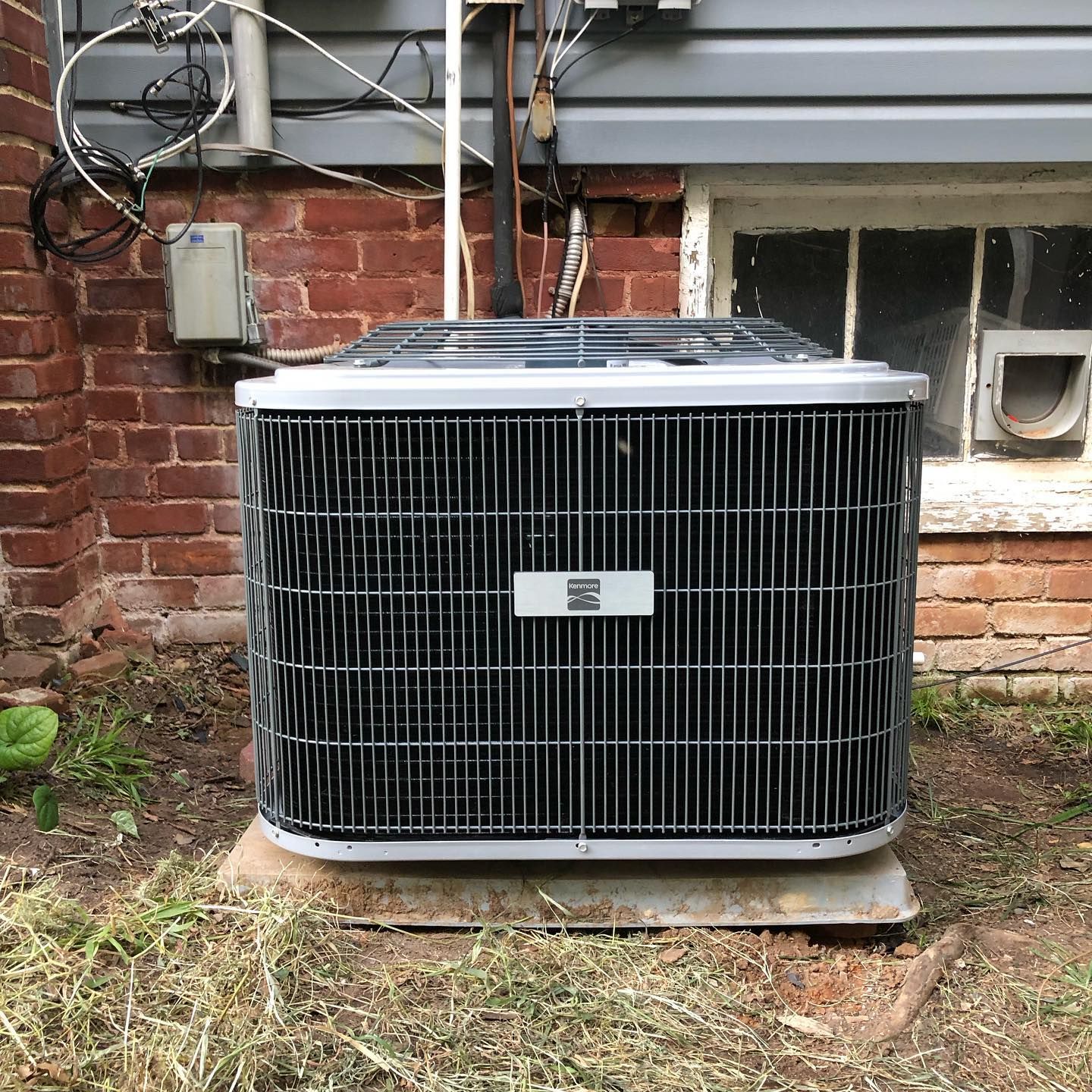 An air conditioner is sitting outside of a brick building.