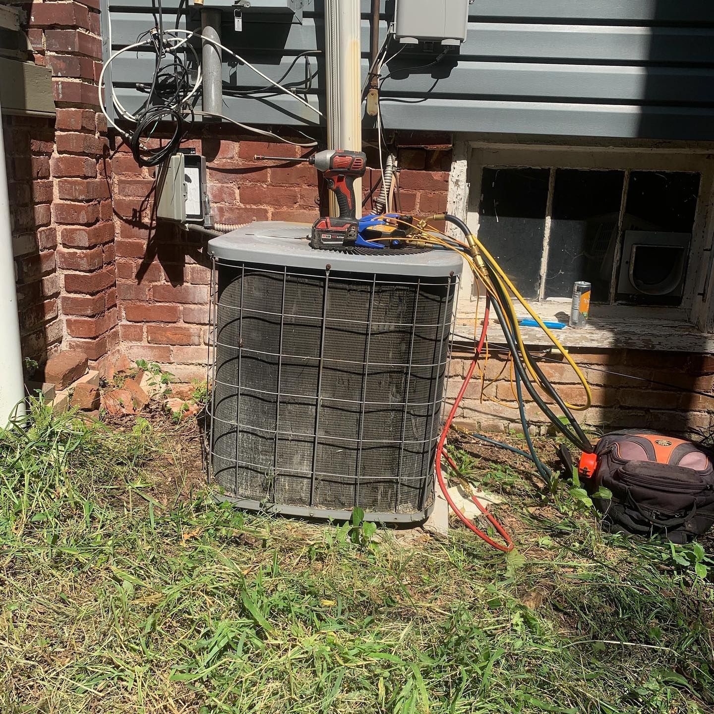 An air conditioner is sitting in the grass in front of a brick building.