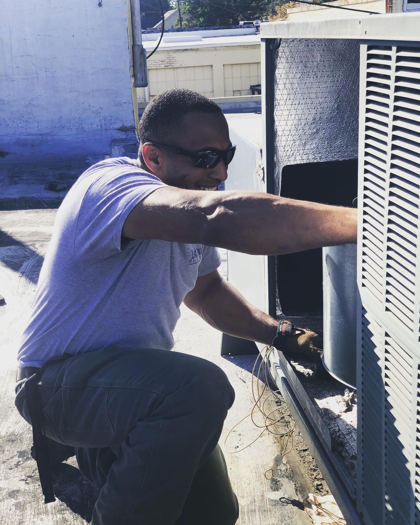 A man wearing sunglasses is working on an air conditioner