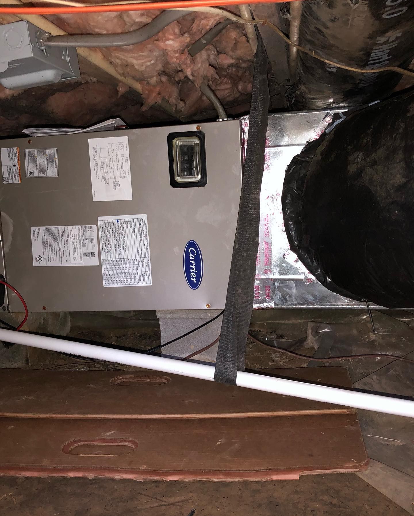 A carrier air conditioner is sitting under a ceiling in a basement.