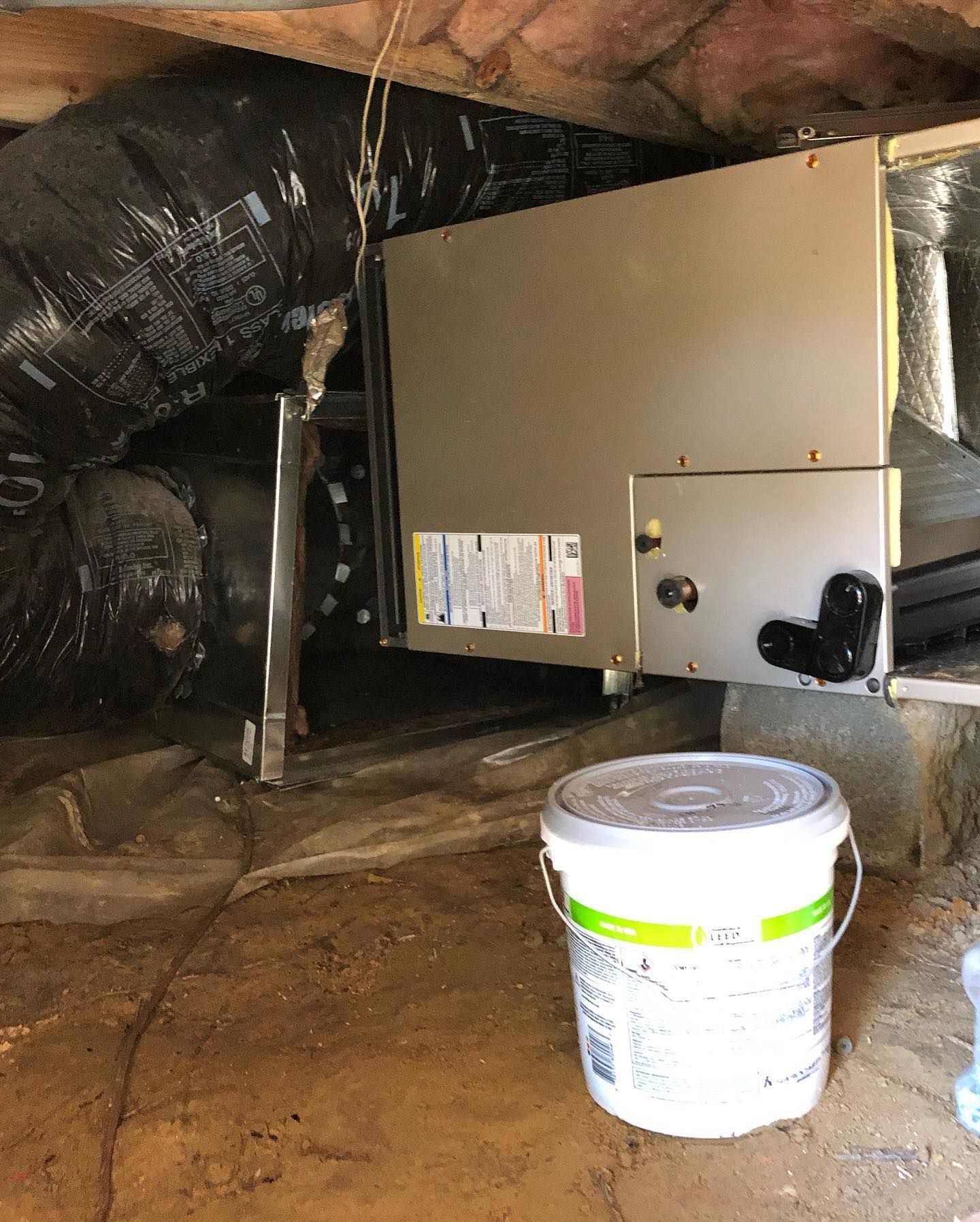 A bucket of paint is sitting next to a machine in a basement.