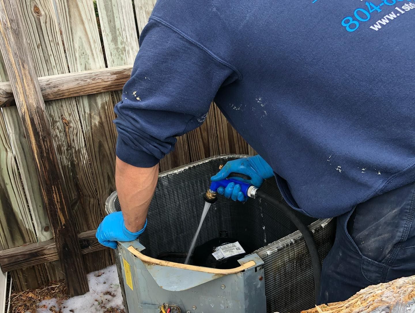 A man is cleaning an air conditioner with a hose.