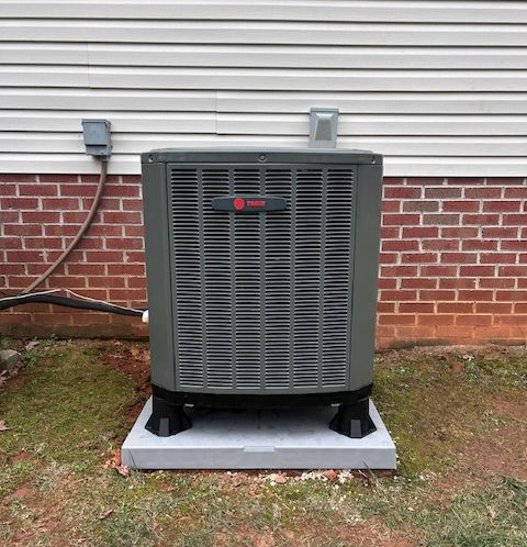 An air conditioner is sitting in the grass next to a hose.