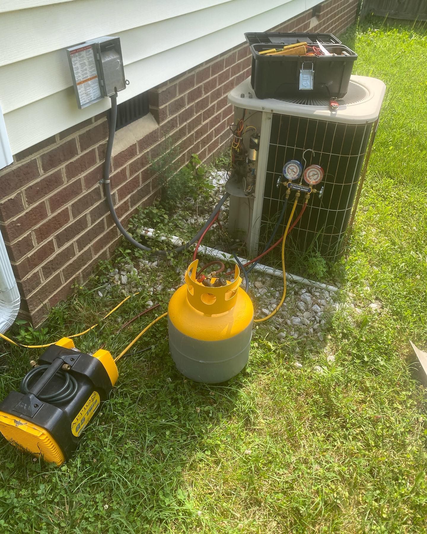 A propane tank is sitting in the grass next to an air conditioner.