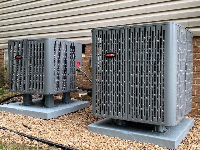 Two air conditioners are sitting on top of gravel in front of a brick building.