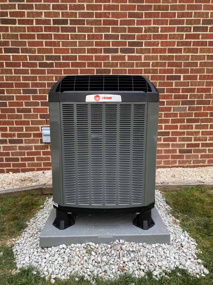 A large air conditioner is sitting on top of a pile of gravel in front of a brick wall.