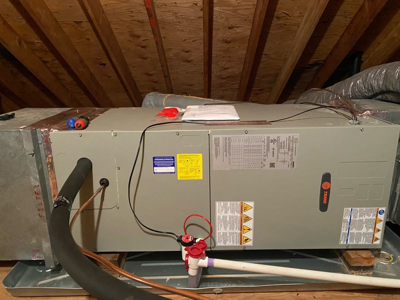 A large air conditioner is sitting on top of a wooden floor in an attic.