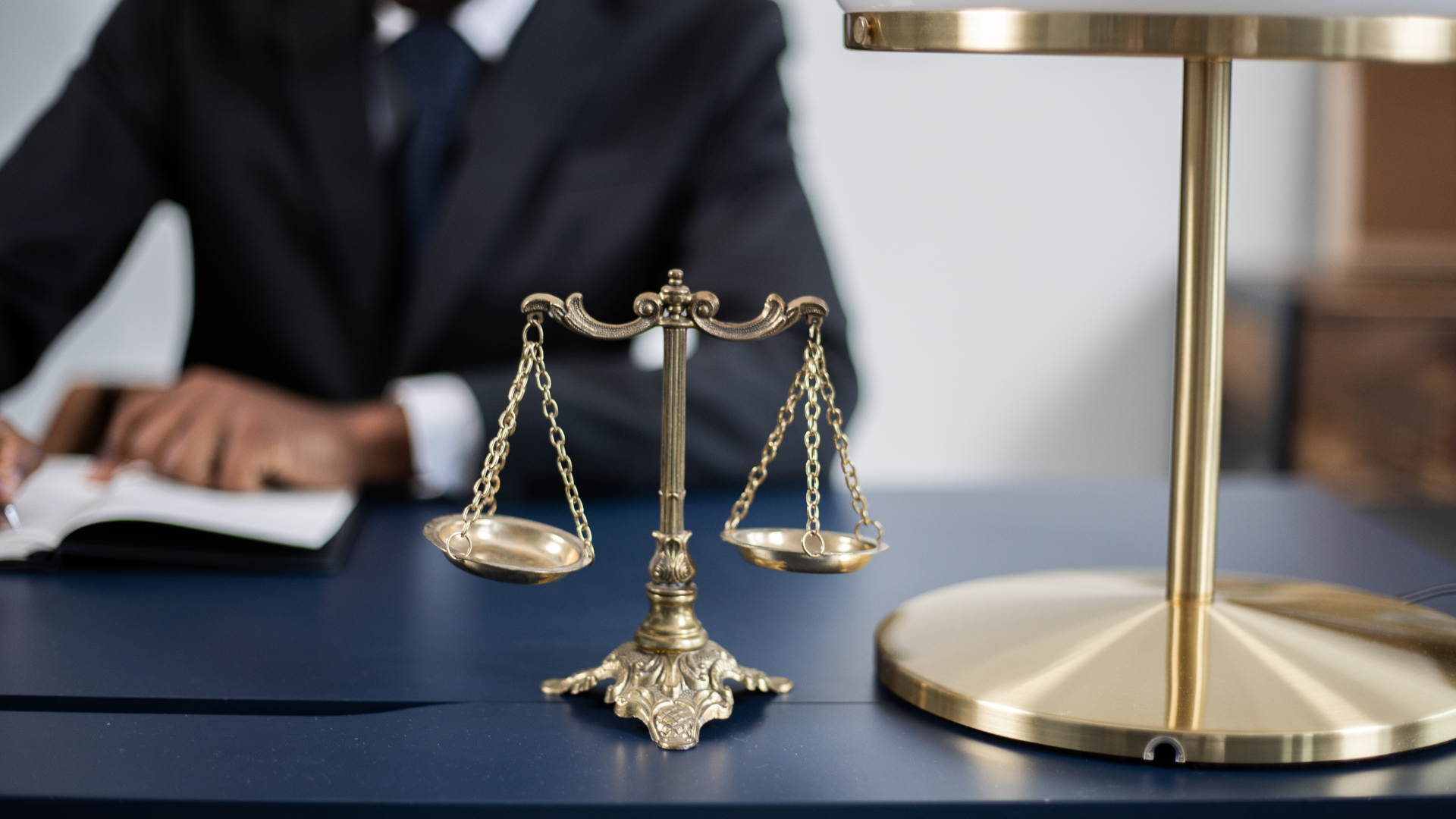 Scales of justice on desk, a lawyer in suit writing, focused on legal matters.
