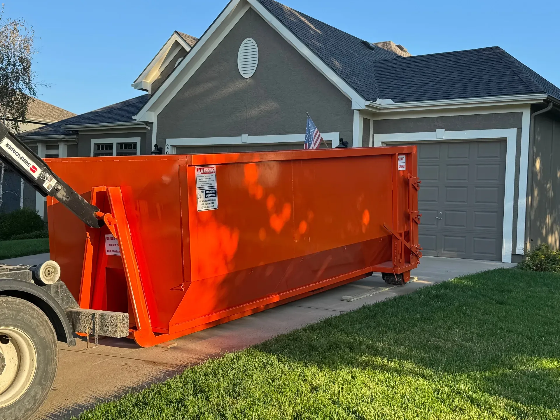 White industrial dumpster with a gray angled lower panel on grass.
