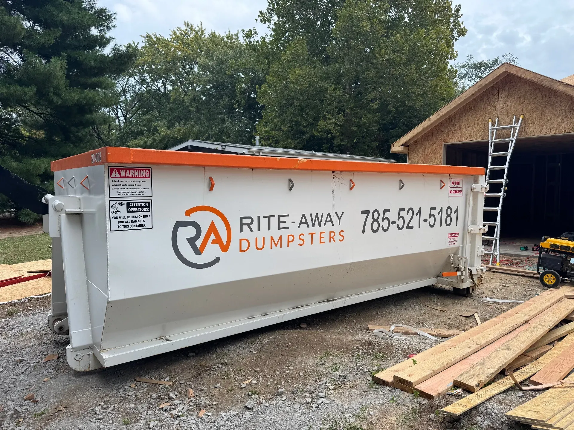 White dumpster on a driveway in front of a house with a basketball hoop.