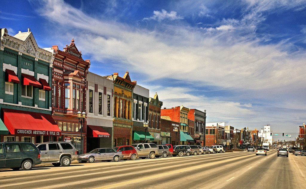 A row of buildings along a street with cars parked on the side of the road.