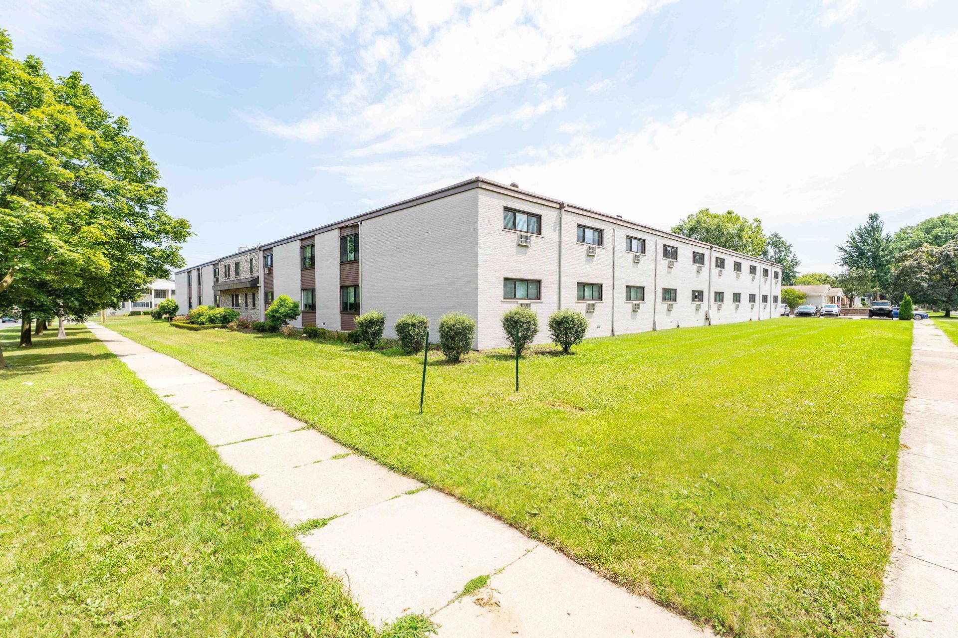 Two-story white apartment building with green lawn and sidewalk on a sunny day.