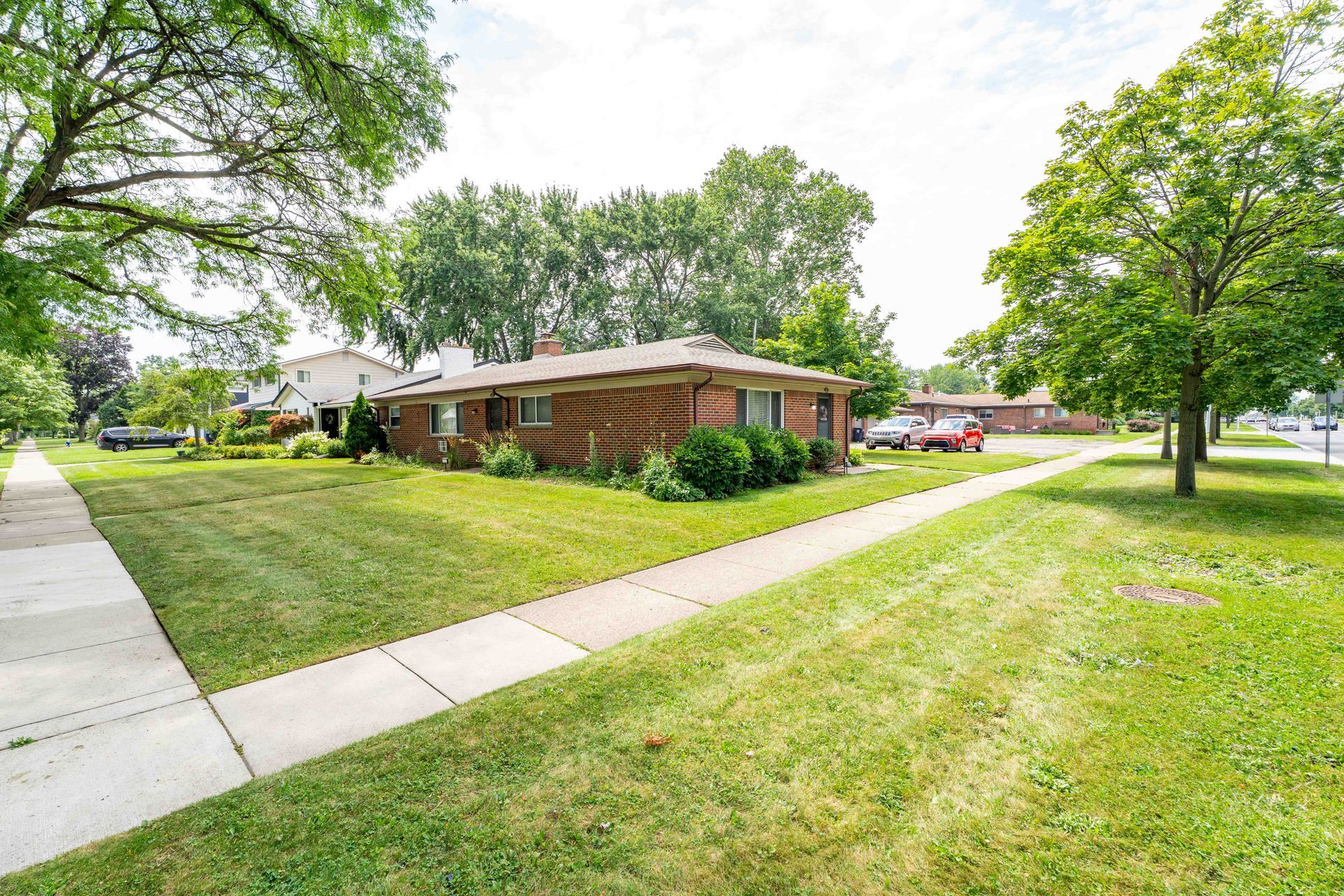 Brick ranch house with green lawn, sidewalk, and trees on a sunny day.