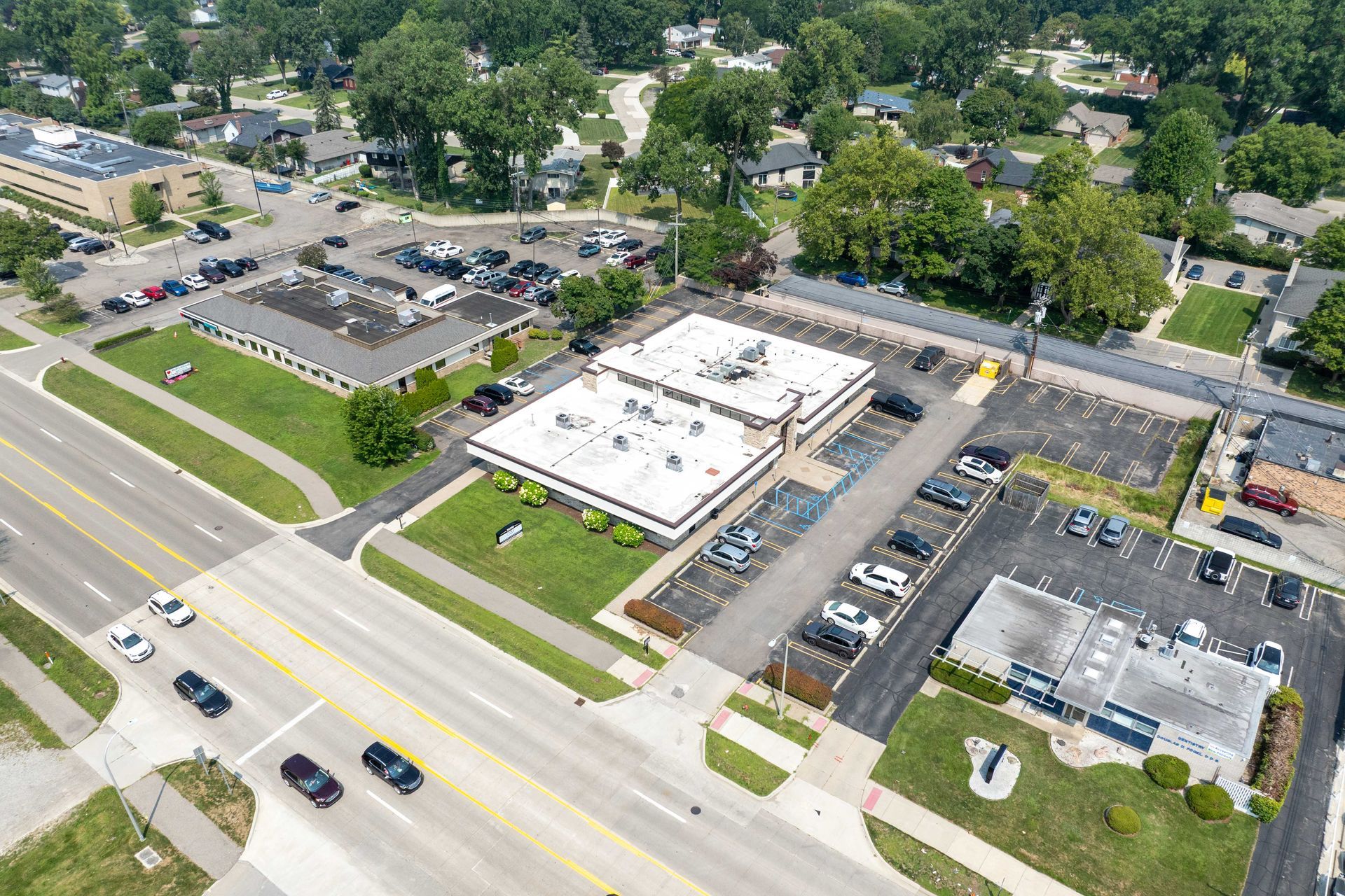 Aerial view of commercial buildings with cars in parking lots, on a street with trees.