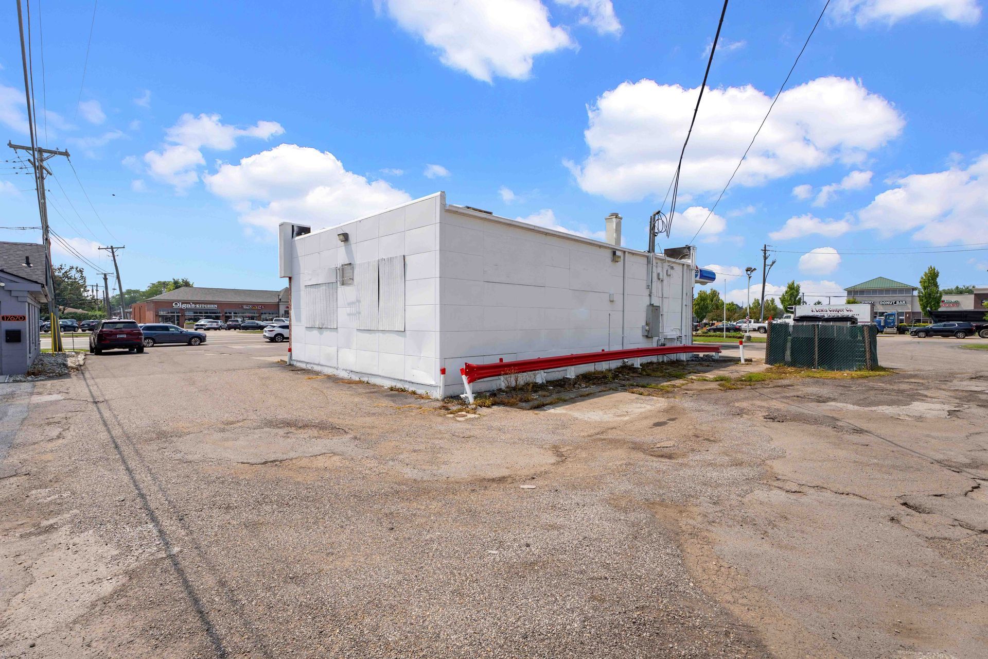 White building with a red stripe on a gravel lot. Blue sky with clouds.