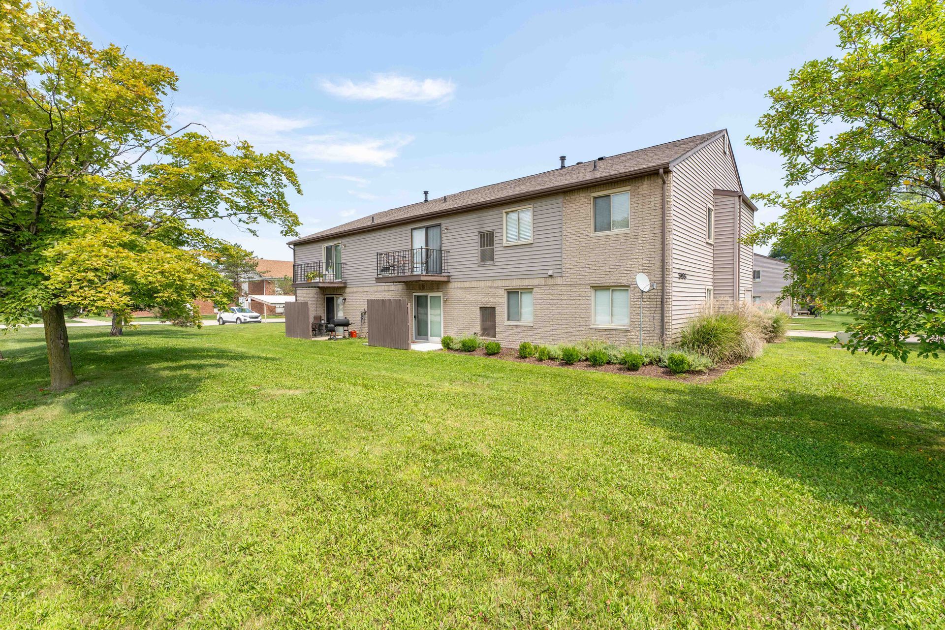 Apartment building exterior with green grass and trees under a blue sky.