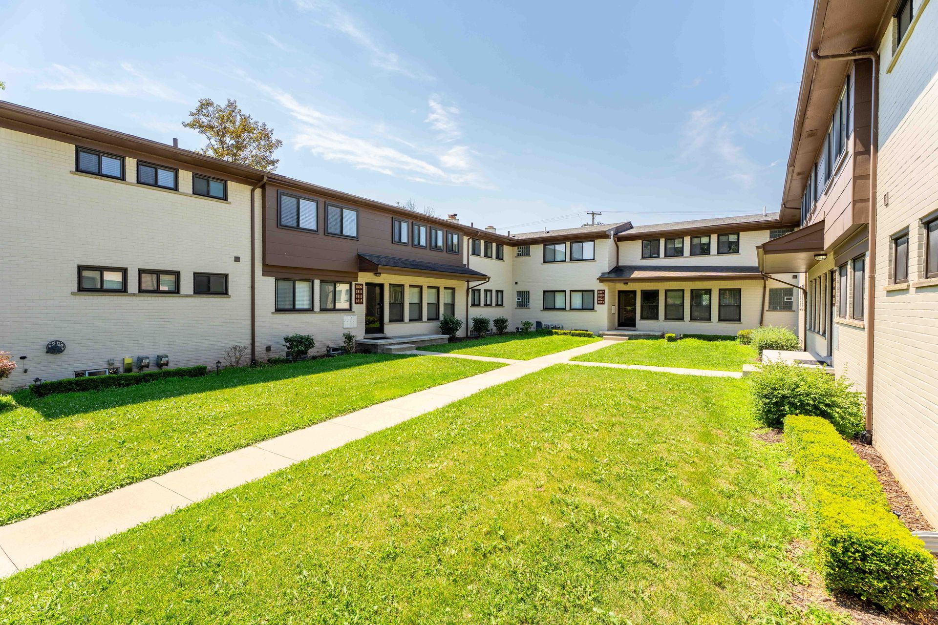 A courtyard with green grass, walkways, and two-story townhouses with beige walls and brown trim on a sunny day.